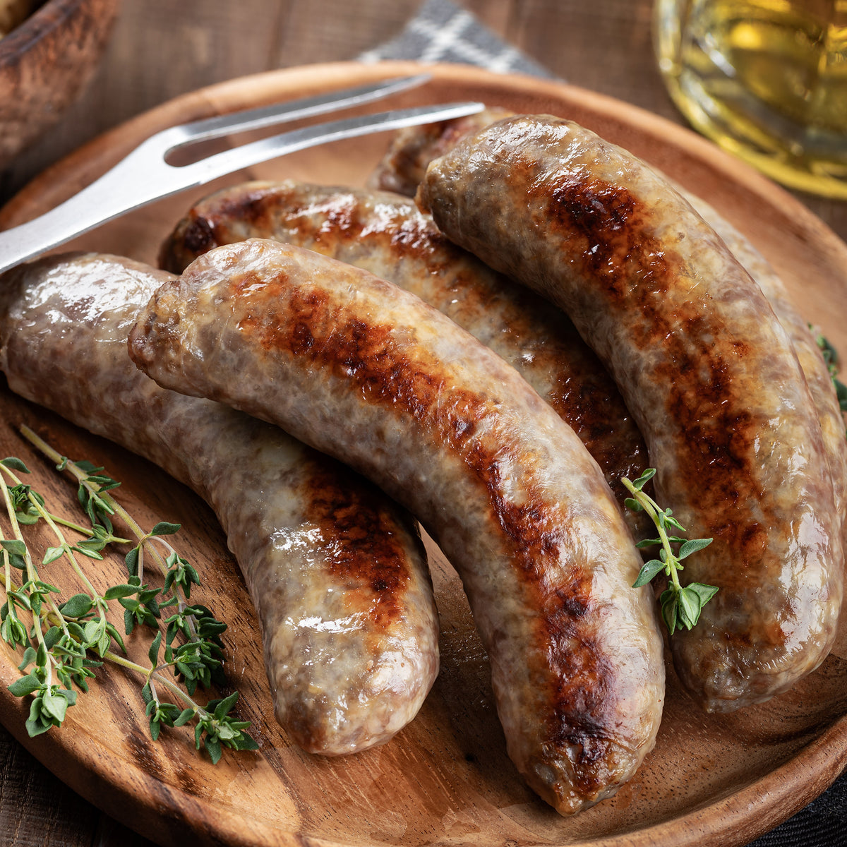 Grilled bratwurst sausages on a wooden platter with fresh thyme and fork