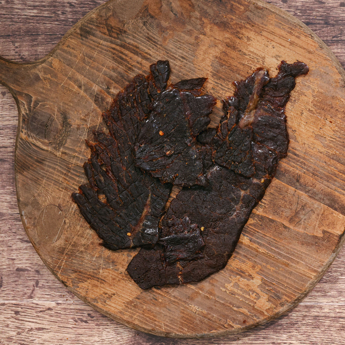 Dark ghost pepper jerky pieces on a rustic wooden board.