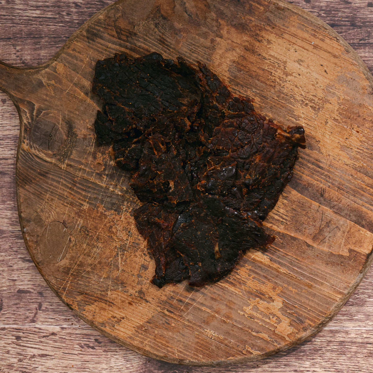 Pieces of dark, marinated beef jerky on an old wooden serving board.