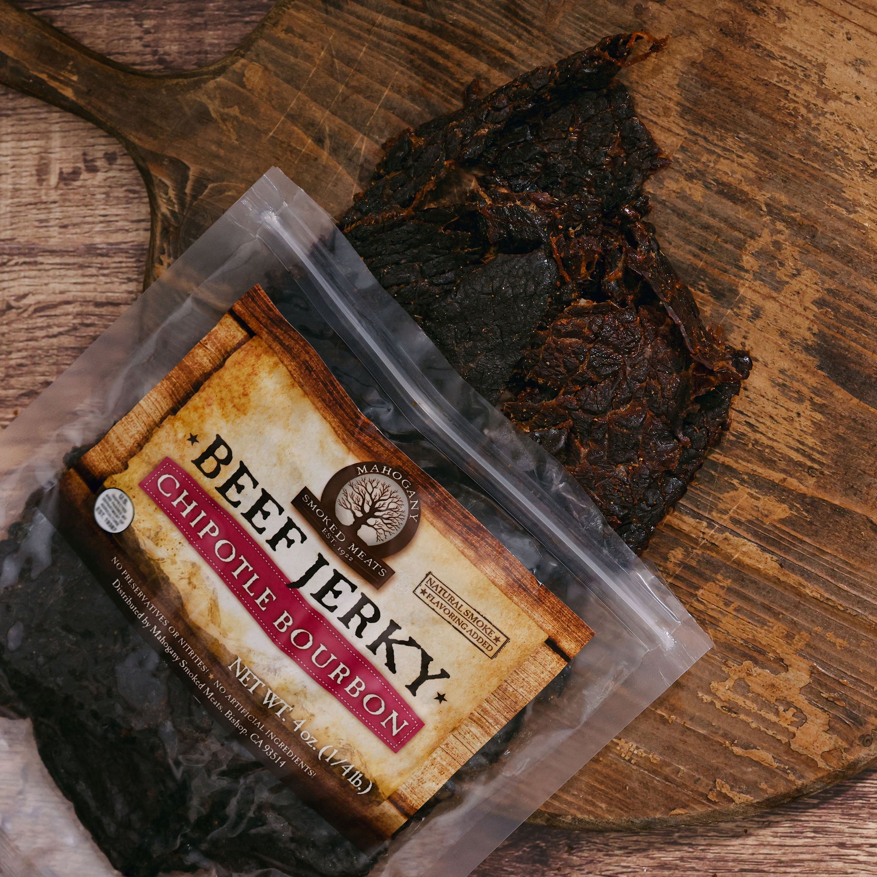 Chipotle bourbon beef jerky on a rustic wooden board with packaging visible.