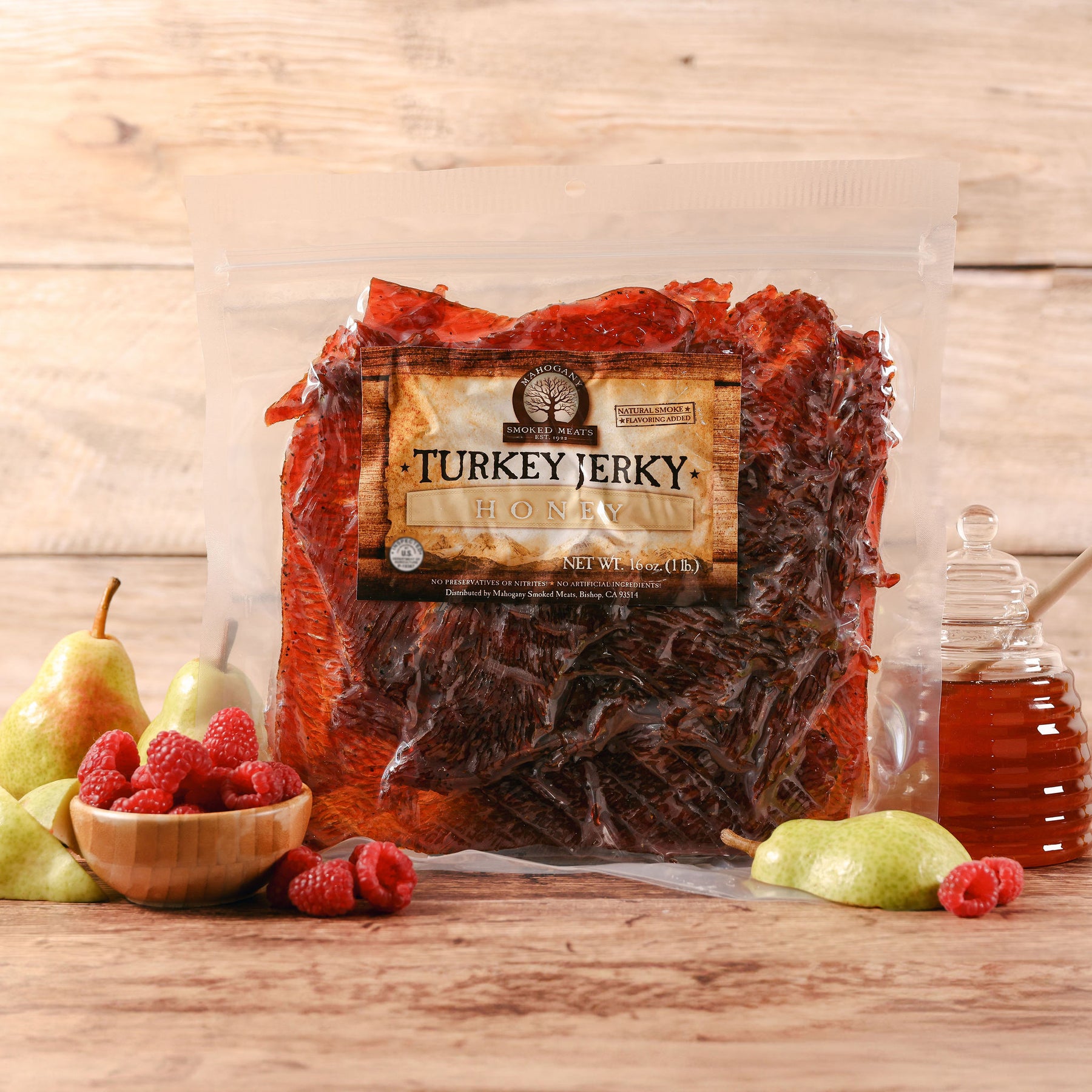 Package of honey turkey jerky displayed with pears, raspberries, and a jar of honey on a wooden surface.