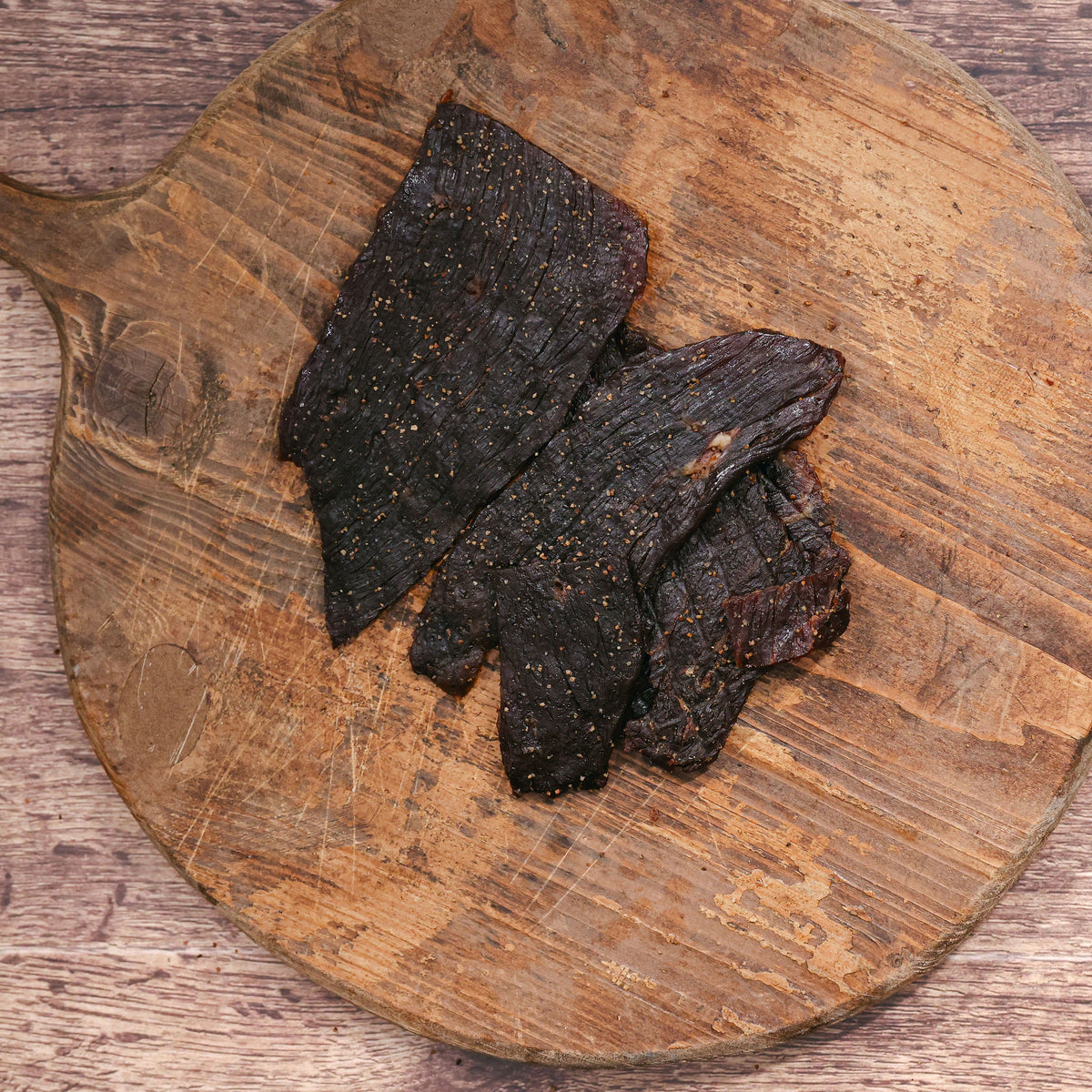 Black peppered buffalo jerky pieces on a rustic wooden cutting board.