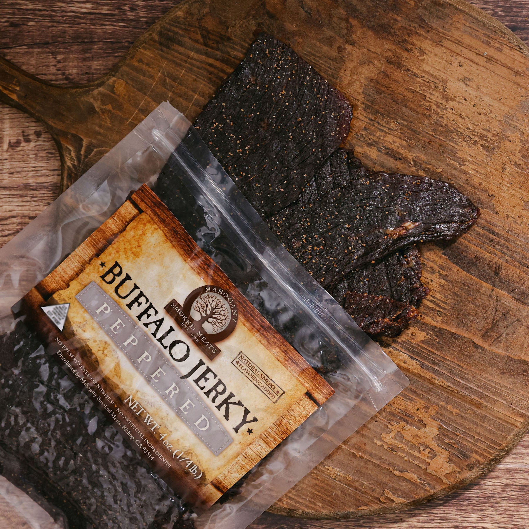 Black peppered buffalo jerky strips on a rustic wooden board with visible packaging.