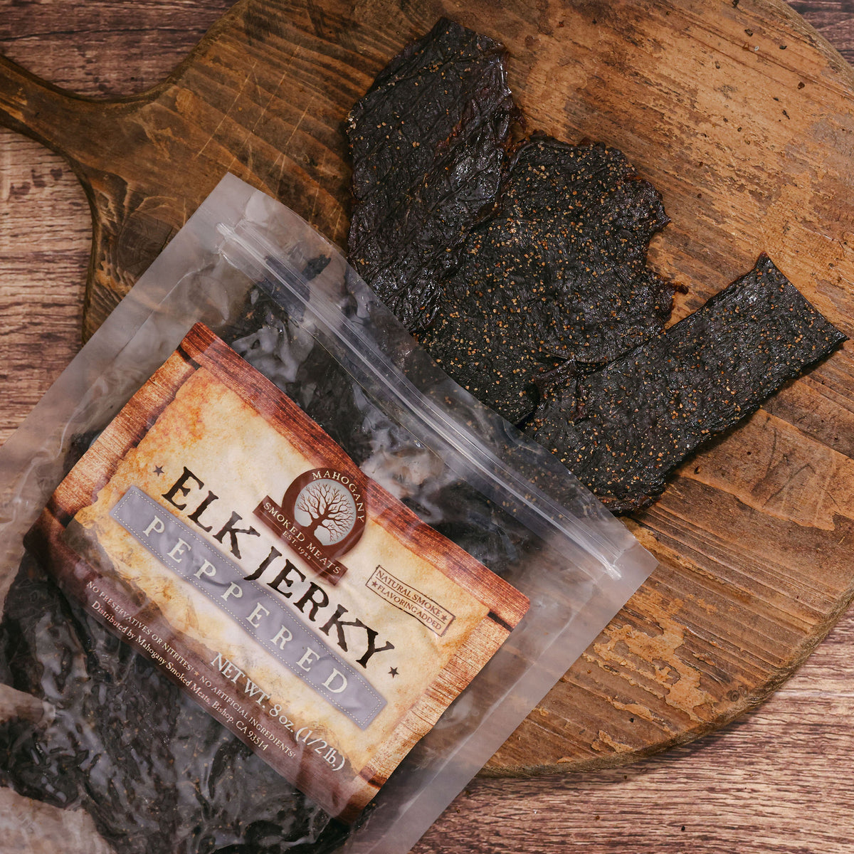 Black peppered elk jerky on wooden board, partially in open package with visible label.