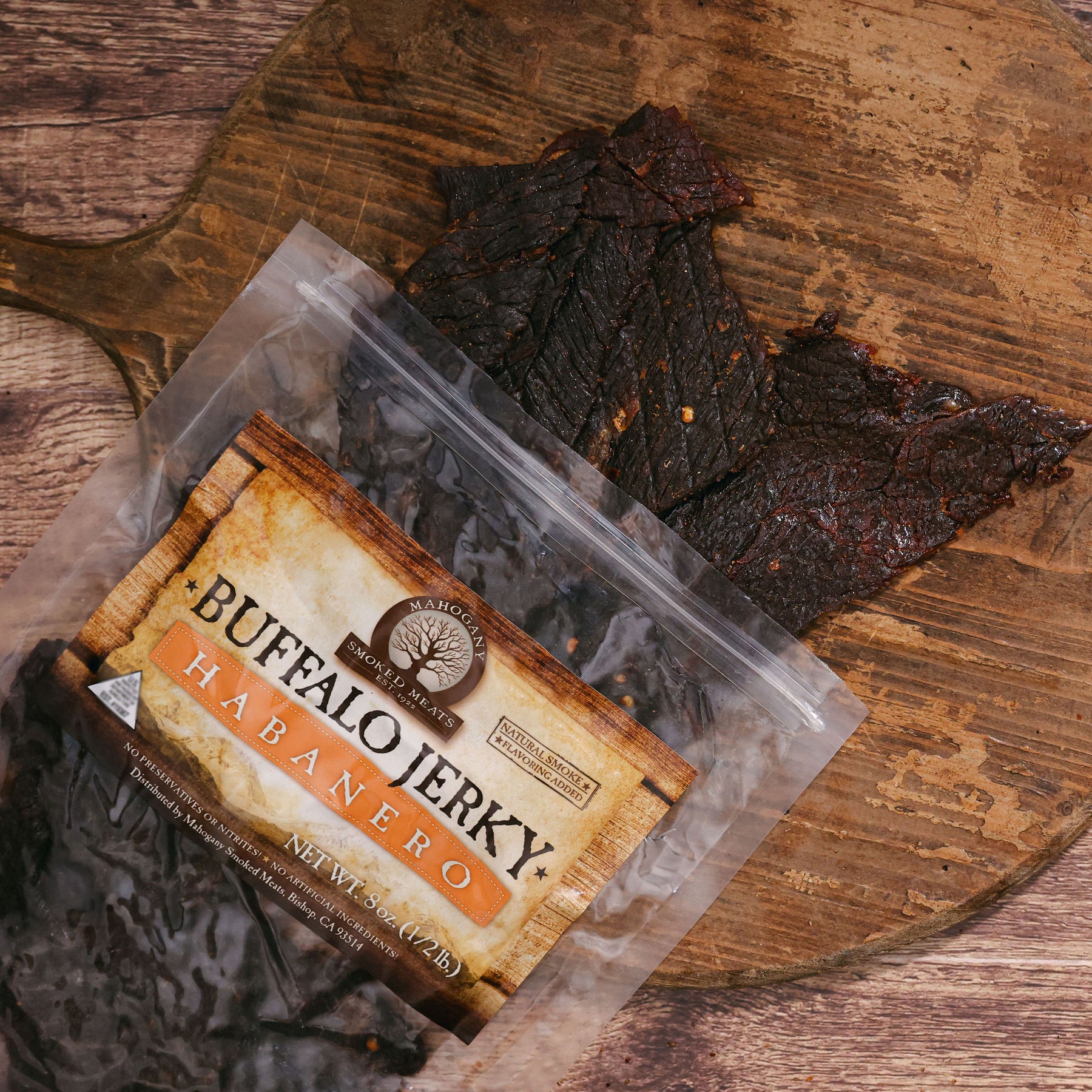 Packaged Habanero Buffalo Jerky on a wooden board, with pieces of jerky outside the bag.