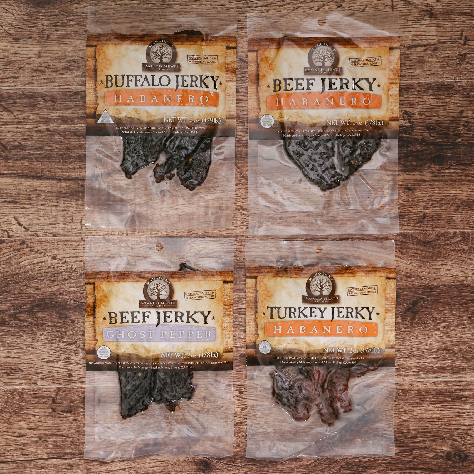 Four packets of jerky on a wooden surface labeled Buffalo, Beef, Beef with Ghost Pepper, and Turkey, all habanero flavored.