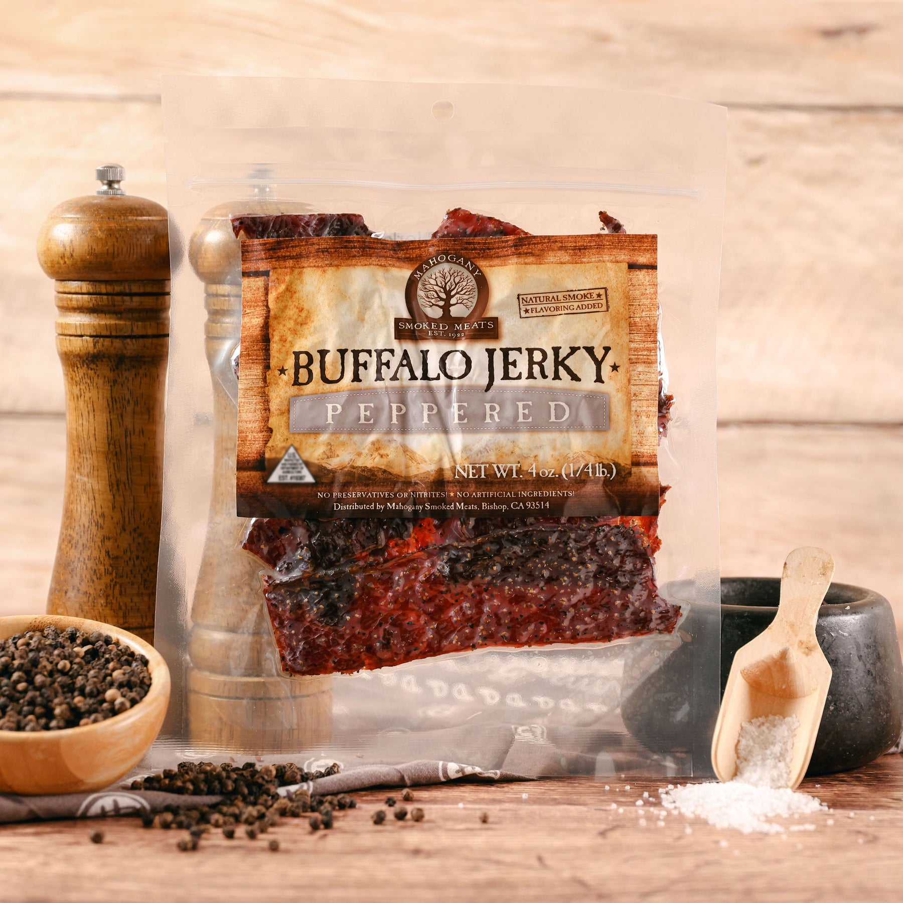 Packaged buffalo jerky with pepper, surrounded by a wooden pepper grinder and bowl of peppercorns.