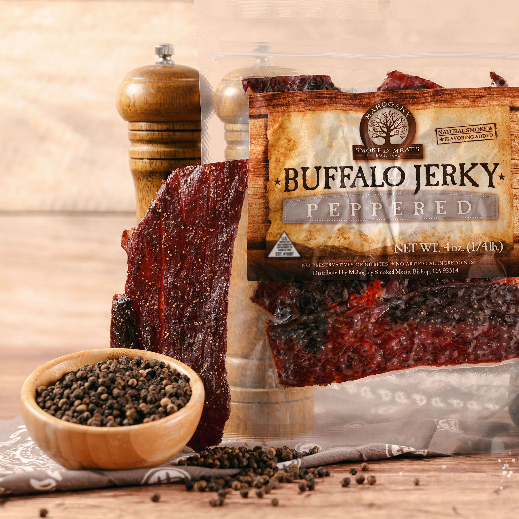 Buffalo jerky strips next to a package with black pepper scattered around, emphasizing the peppered flavor.