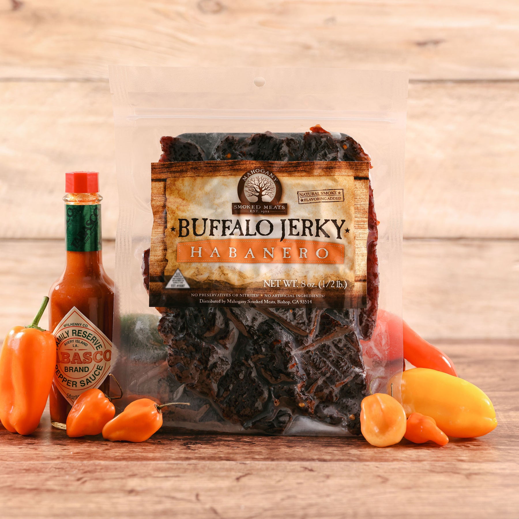 Package of Buffalo Jerky Habanero on a wooden table, accompanied by fresh habanero peppers and a bottle of hot sauce.