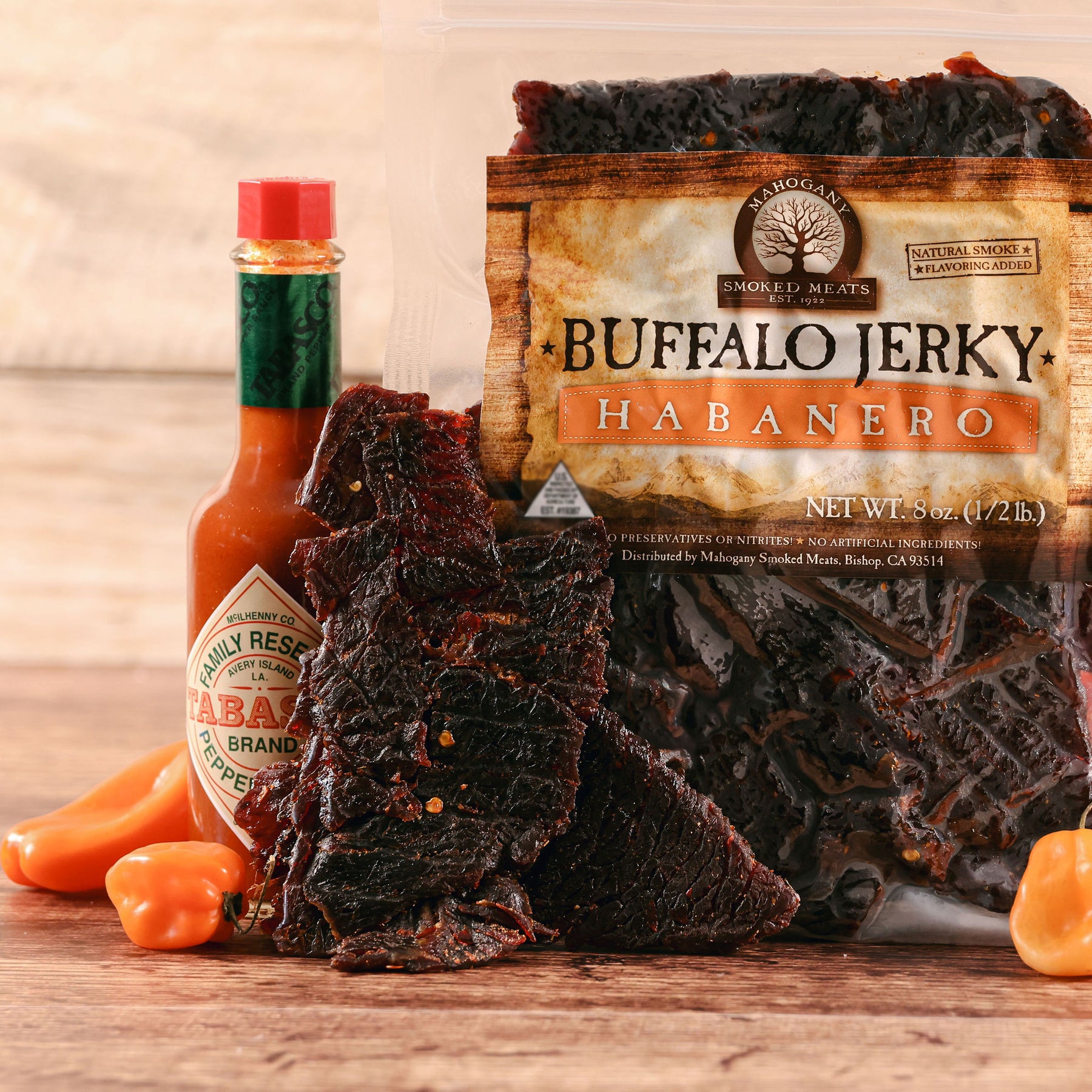 Buffalo jerky and habanero peppers with a bottle of Tabasco sauce on a wooden surface.