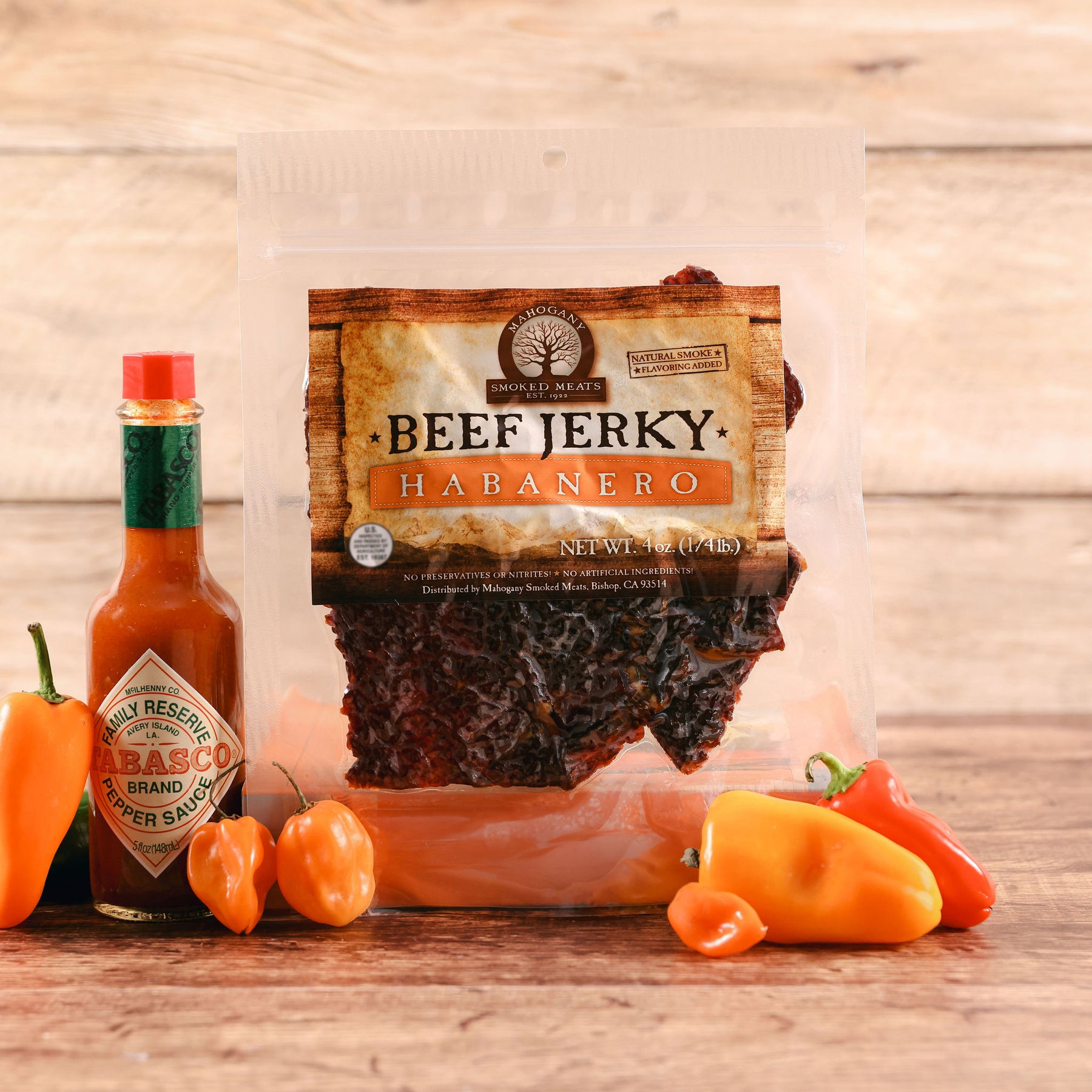 Package of habanero beef jerky next to Tabasco sauce and fresh peppers on wooden table.