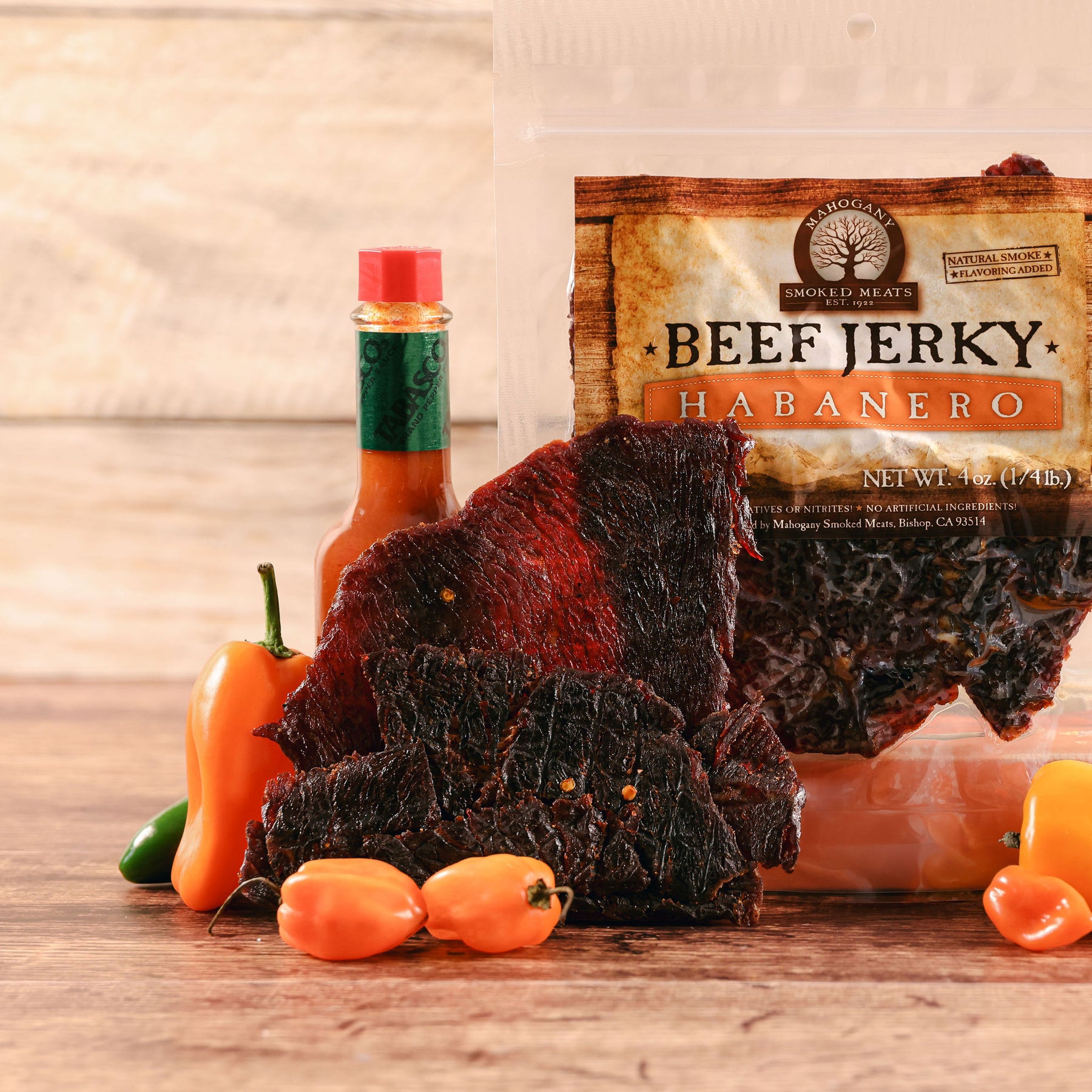 Habanero beef jerky displayed with fresh peppers and a sauce bottle on a wooden surface.
