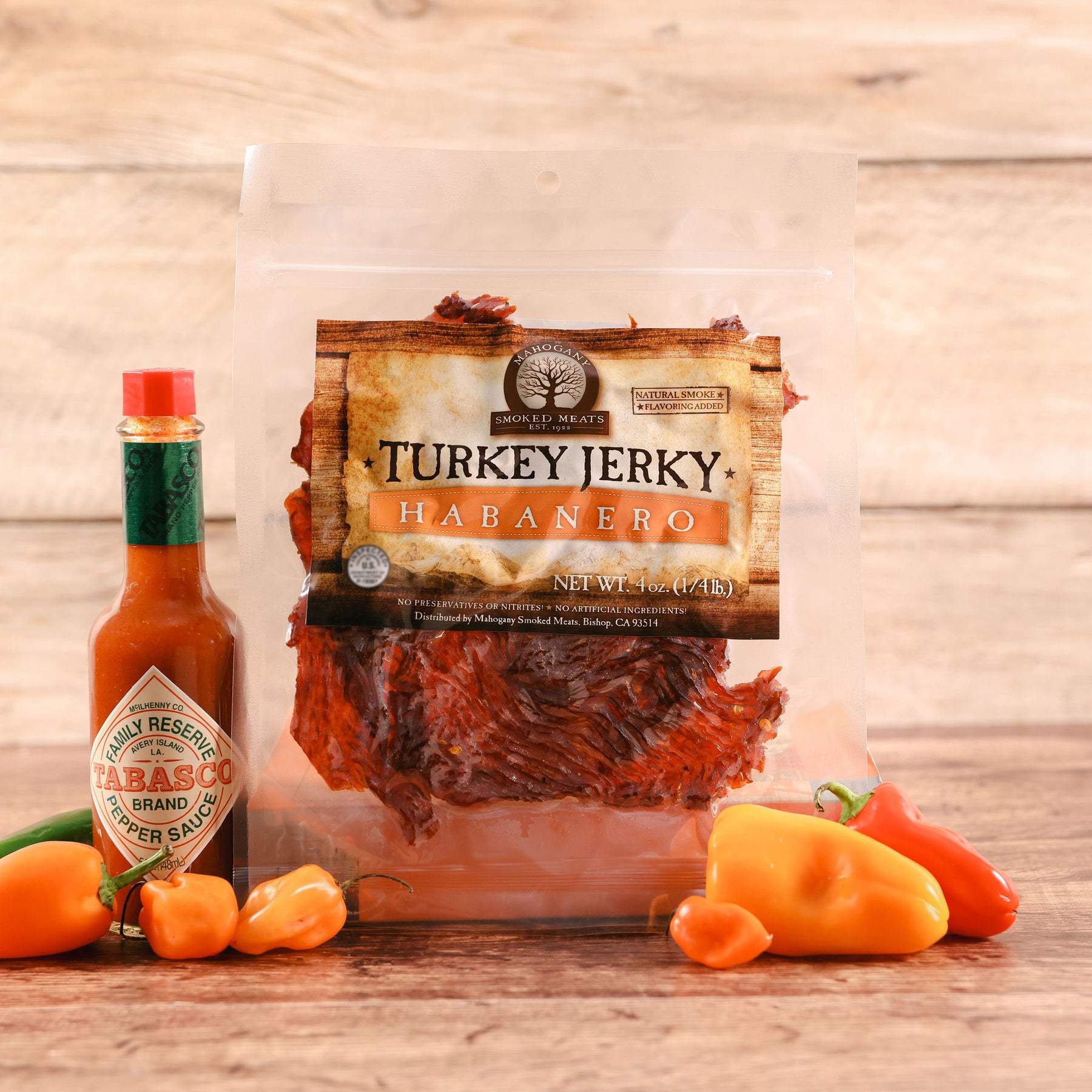 Package of Habanero Turkey Jerky next to Tabasco sauce and fresh habanero peppers on a wooden table