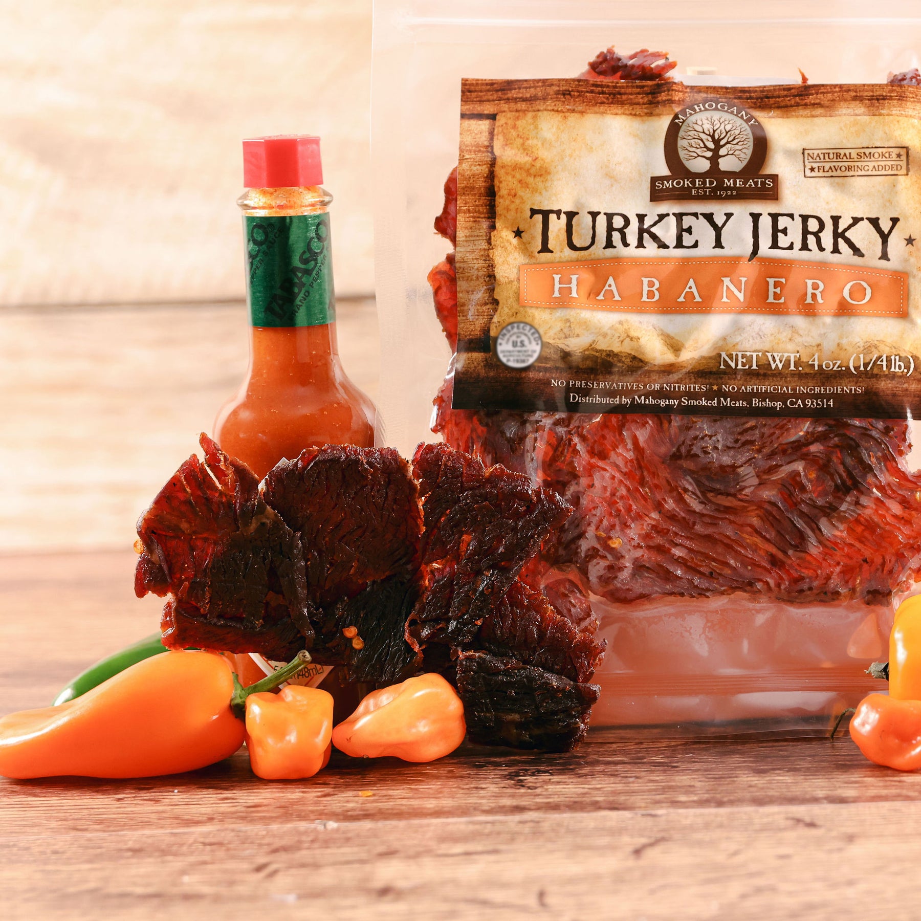 Habanero turkey jerky next to fresh peppers and a bottle of hot sauce on a wooden surface.