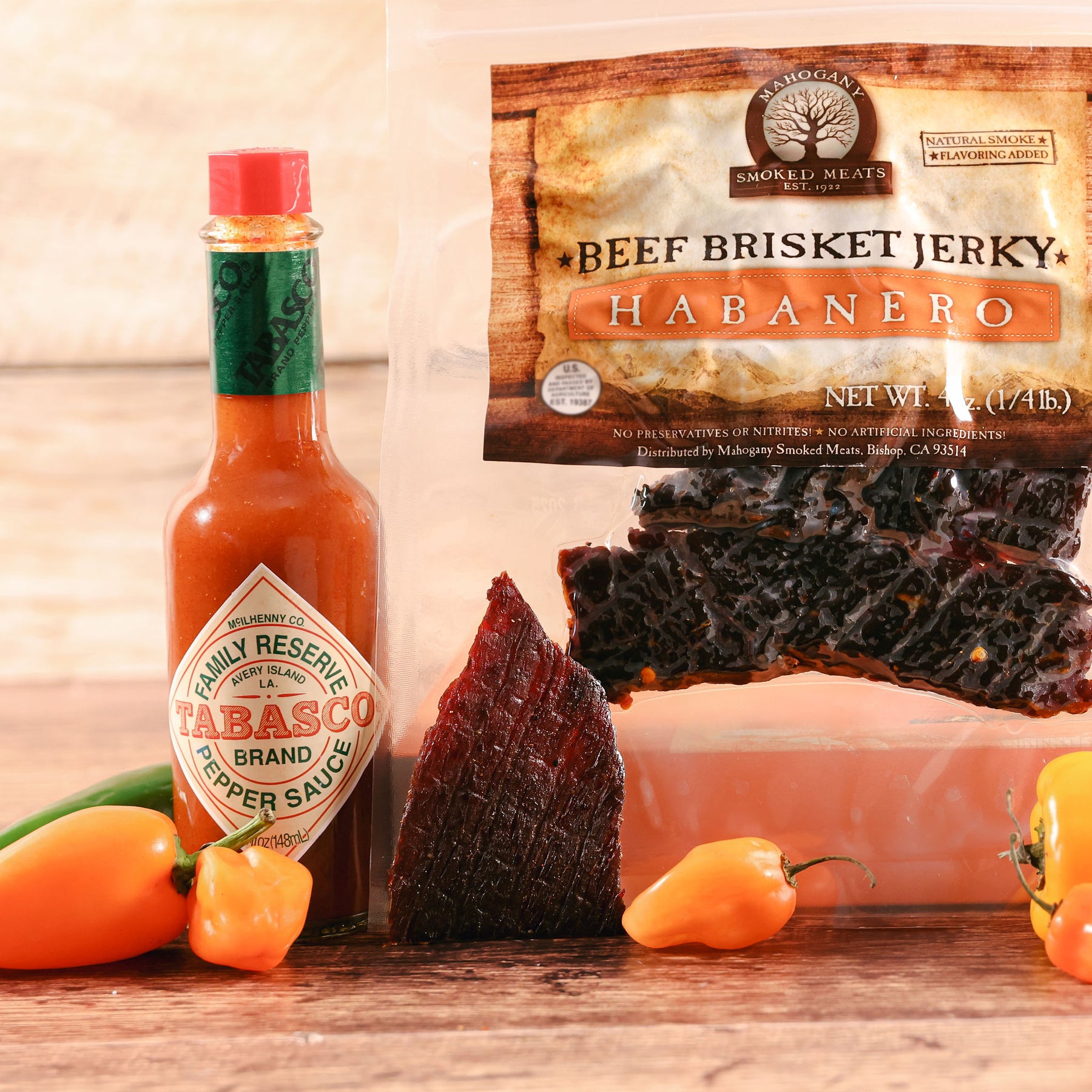 Beef brisket jerky and Tabasco sauce with fresh habanero peppers on a wooden table.