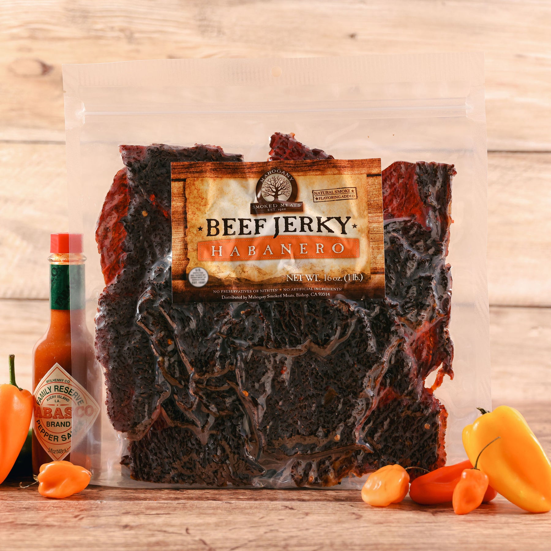 Packaged habanero beef jerky beside Tabasco sauce and fresh habanero peppers on a wooden surface.