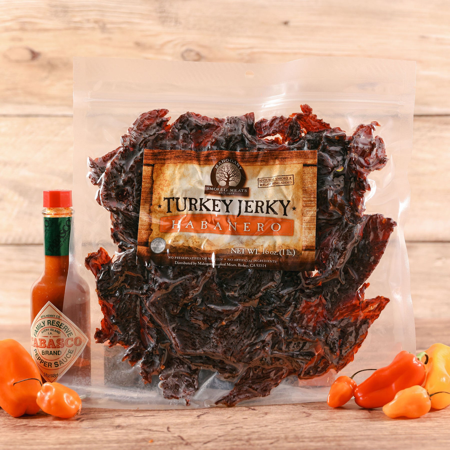 Transparent package of Habanero Turkey Jerky with a small bottle of Tabasco and habanero peppers on a wooden surface.