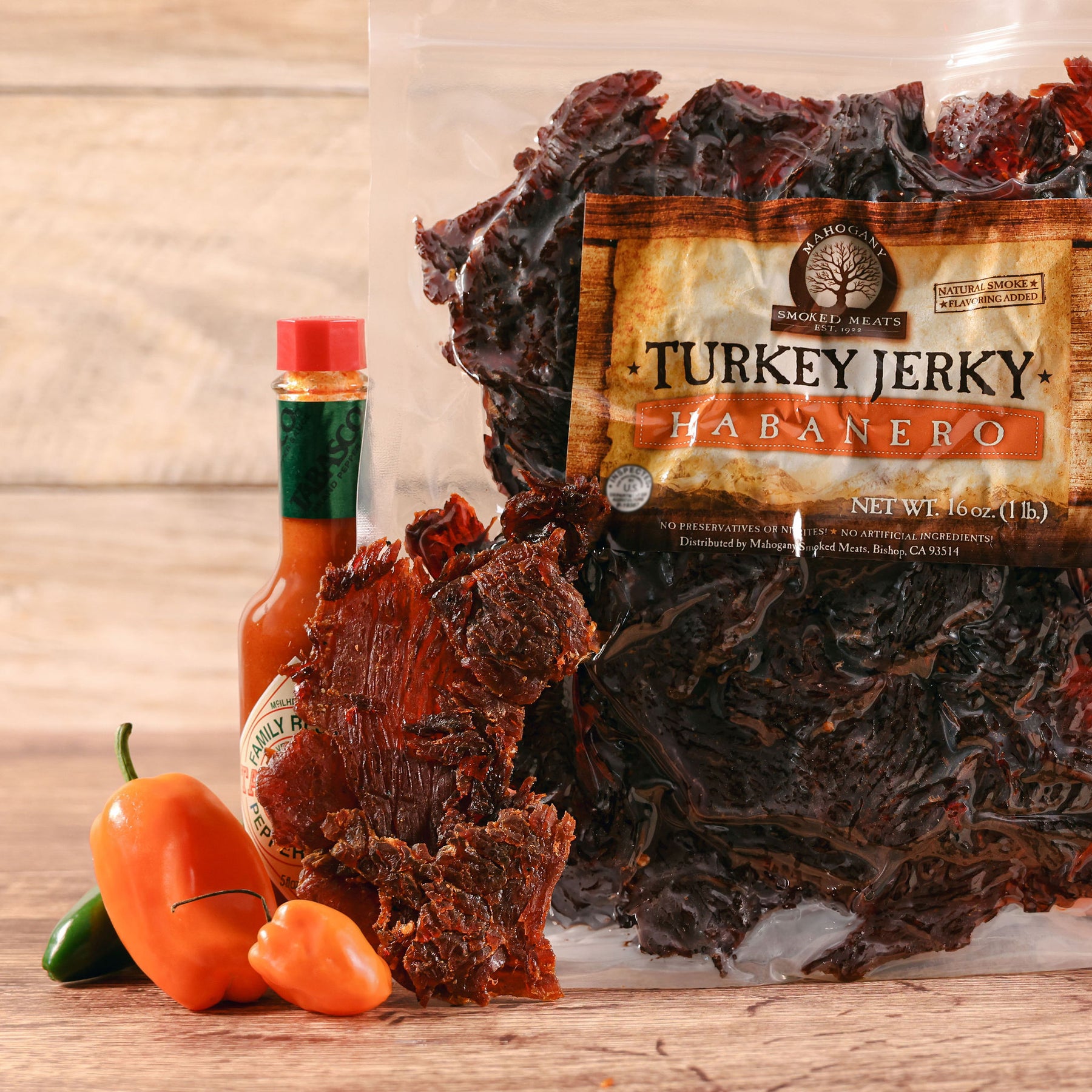 Bag of habanero turkey jerky with a hot sauce bottle and fresh habanero peppers on a wooden surface.