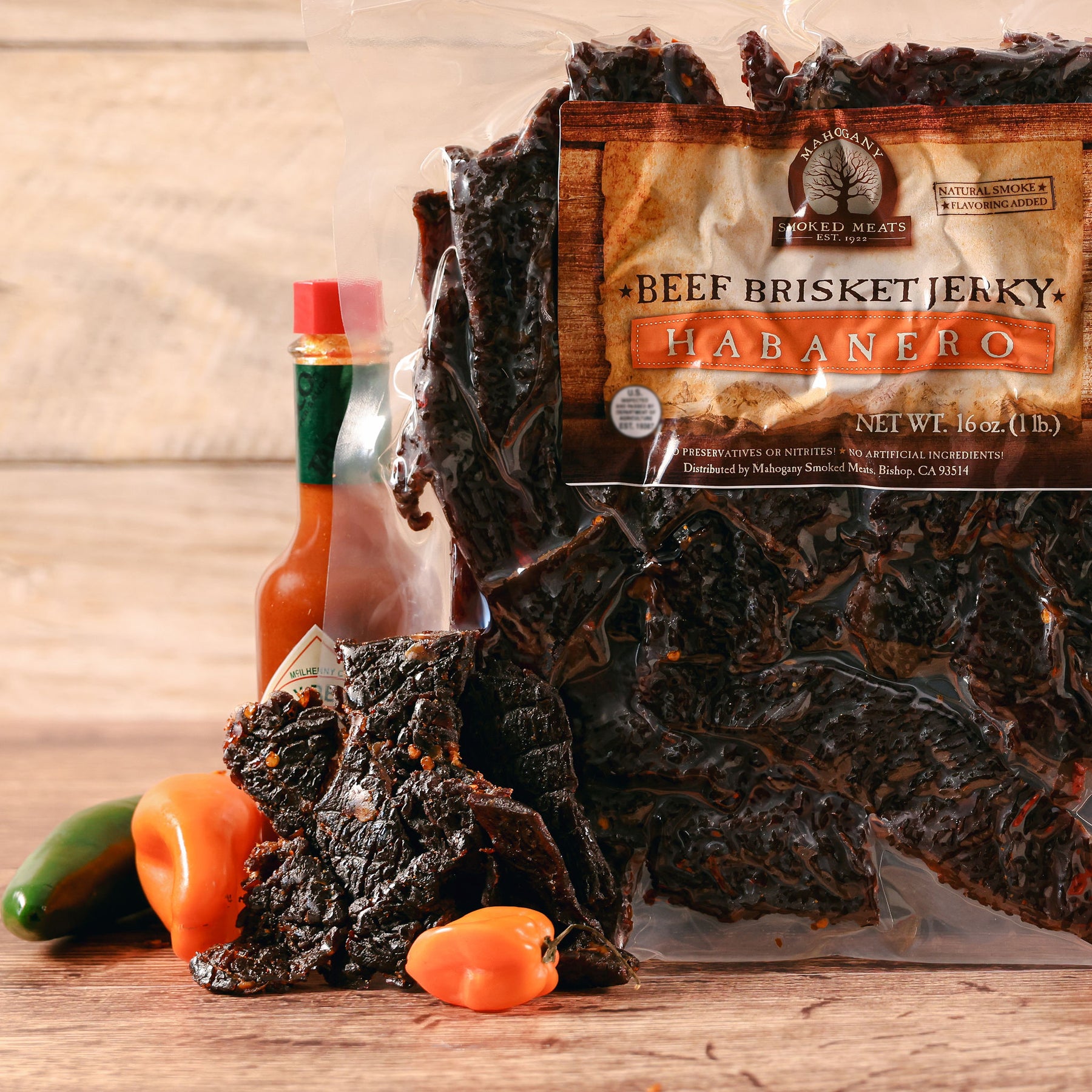 Beef brisket jerky labeled "Habanero" with hot sauce and fresh peppers on a wooden surface.
