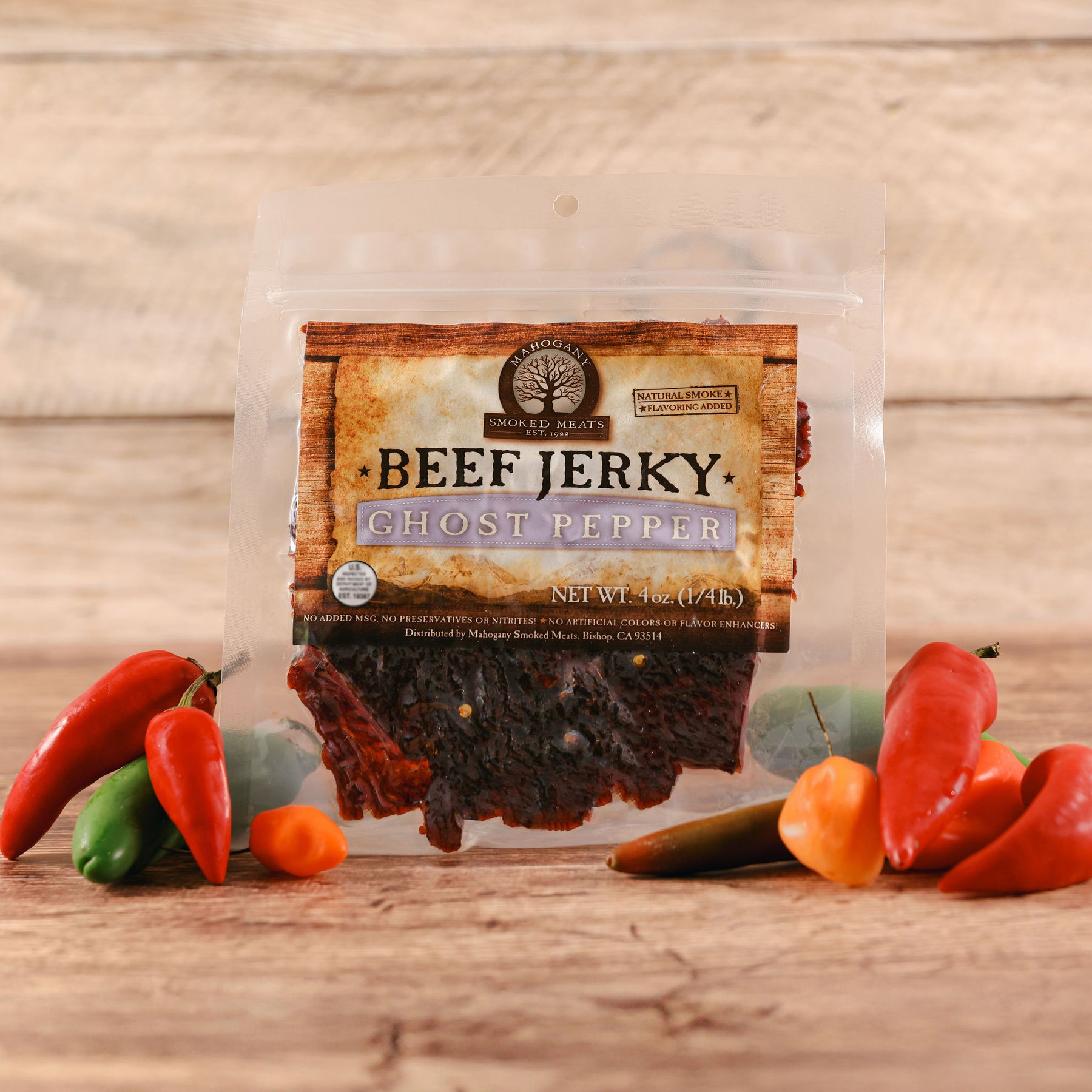 Beef jerky pack labeled 'Ghost Pepper' surrounded by colorful chili peppers on a wooden surface.