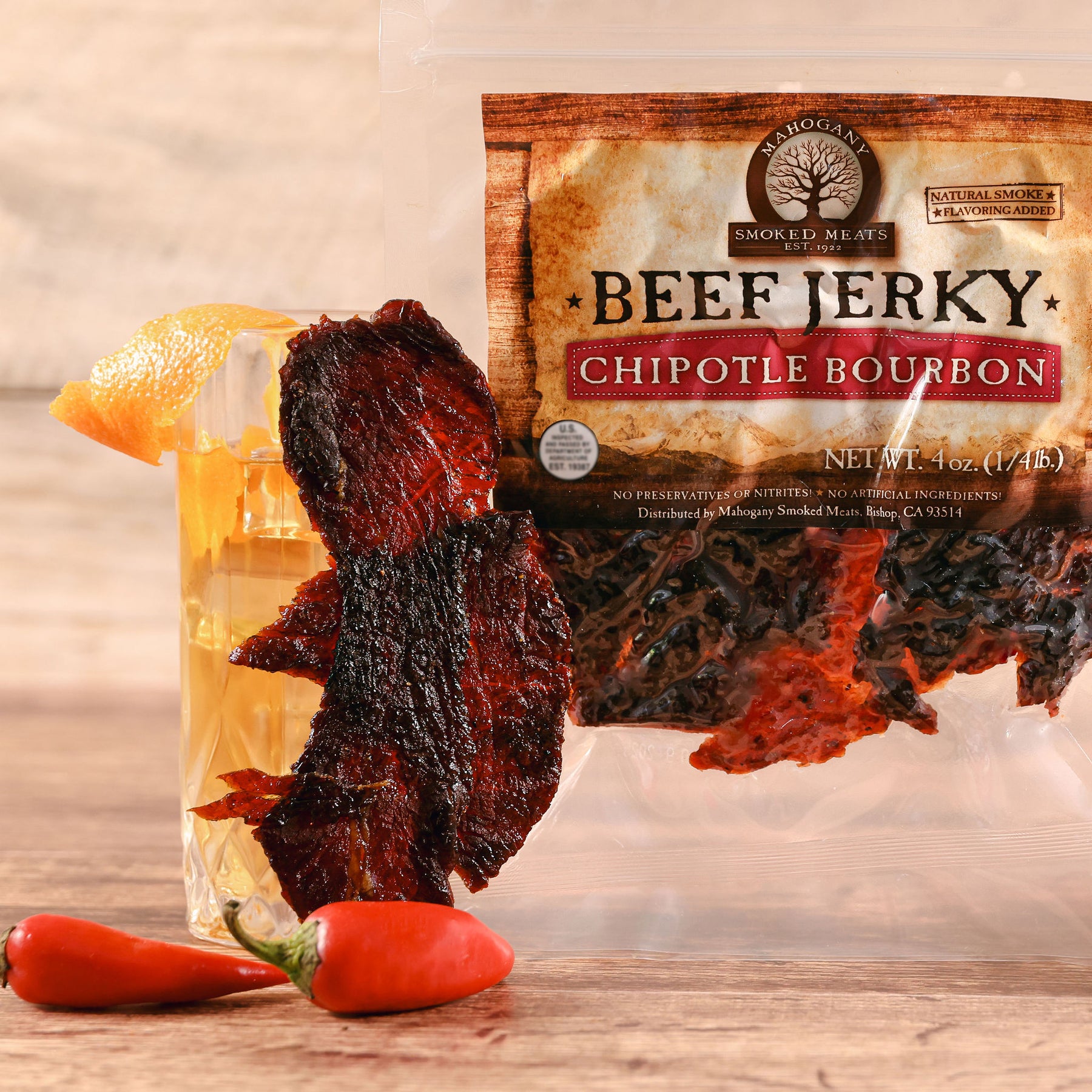 Pack of Chipotle Bourbon Beef Jerky with red chili peppers, displayed on a wooden surface.