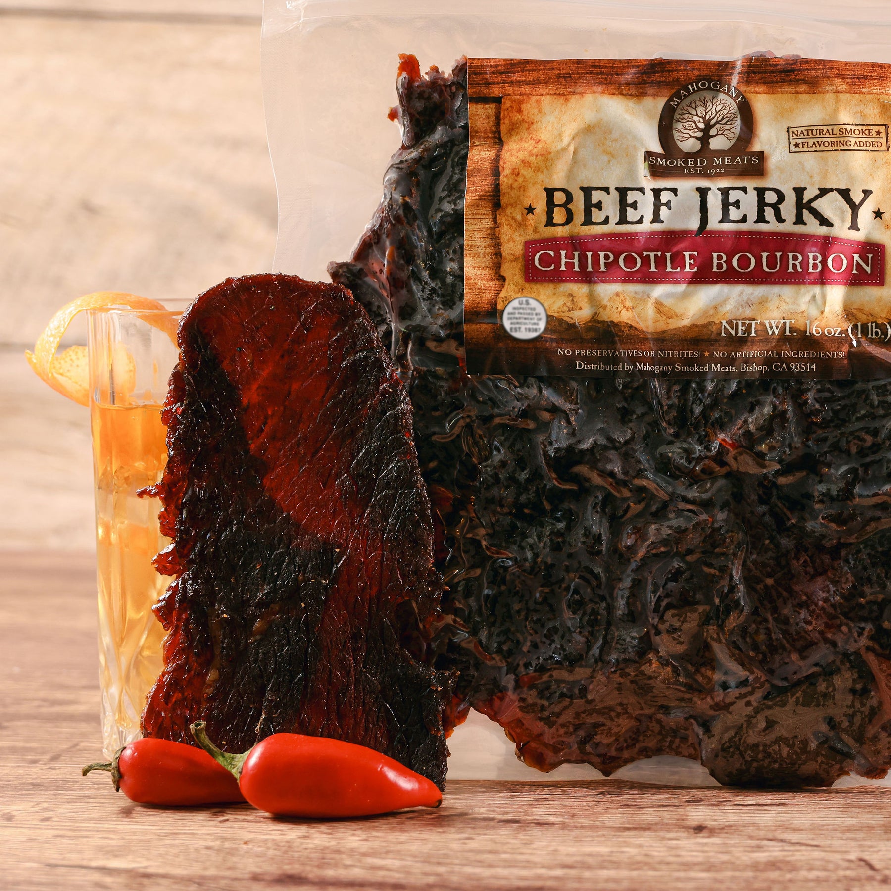 Chipotle Bourbon Beef Jerky package with slices of jerky, red peppers, and wooden backdrop.