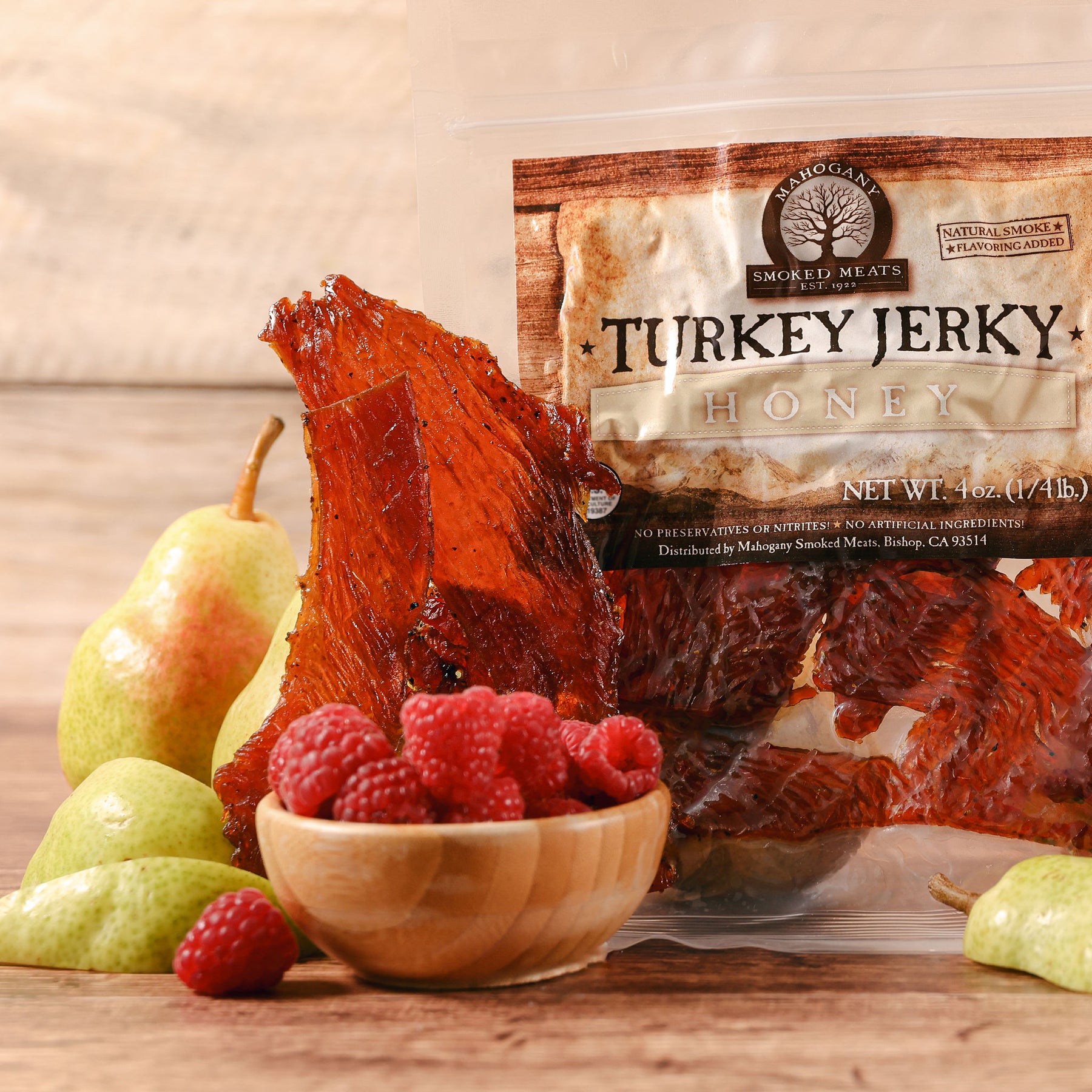 Glistening honey turkey jerky displayed beside a bowl of raspberries and pears on a wooden surface.