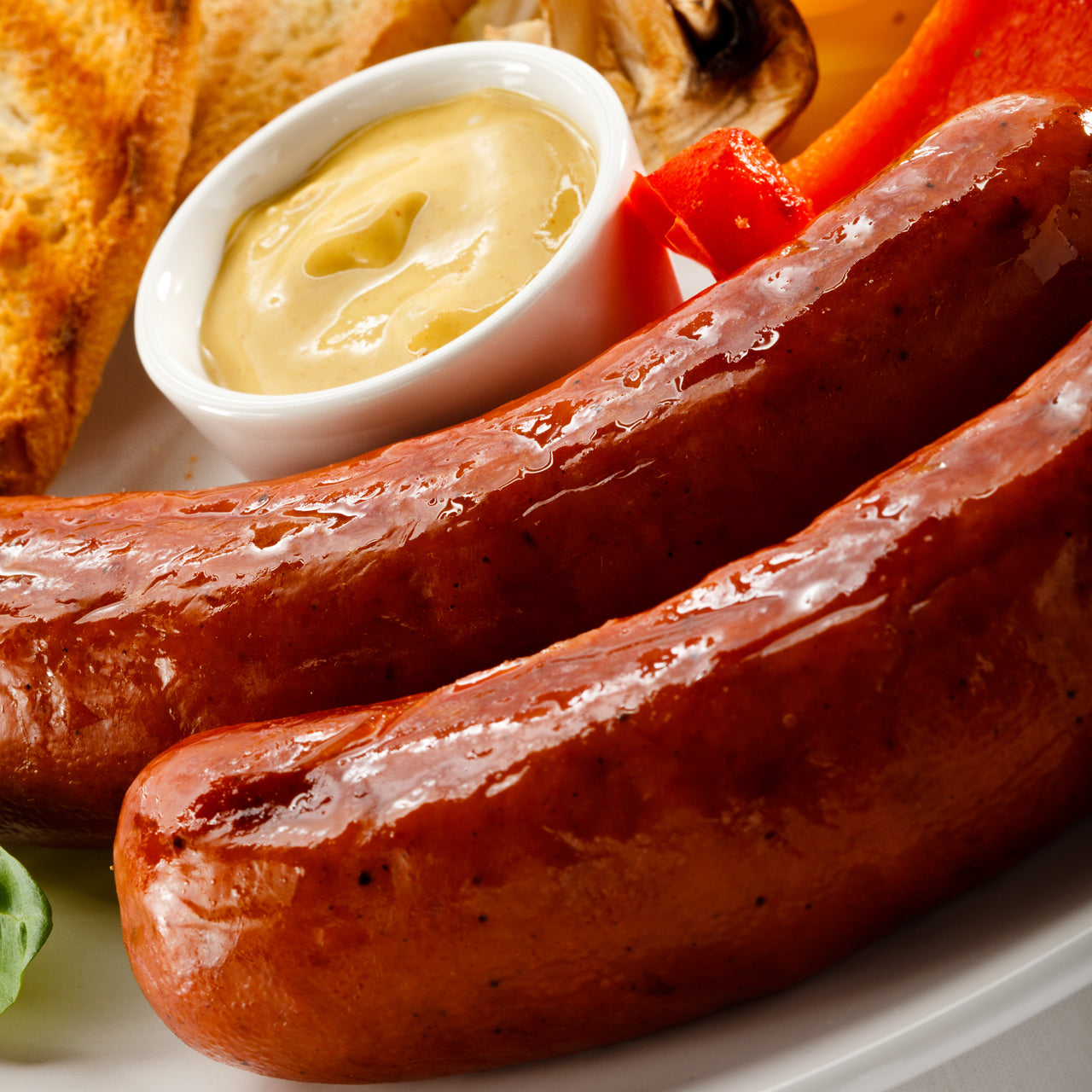 Grilled kielbasa sausages on a plate with mustard, toast, and fresh vegetables.