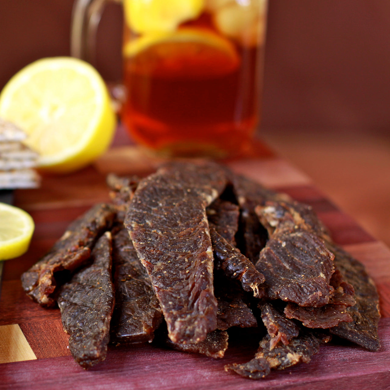 Slices of sweet and spicy brisket on a wooden board, with lemon and iced tea in the background