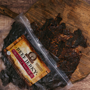 Packaged Chipotle Bourbon Beef Jerky on a rustic wooden board.