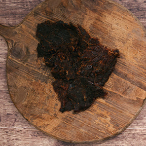 Pieces of dark, marinated beef jerky on an old wooden serving board.