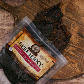 Chipotle bourbon beef jerky on a rustic wooden board with packaging visible.