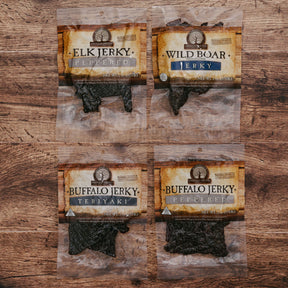 Four packages of exotic meat jerky including elk, wild boar, and buffalo on a wooden table.