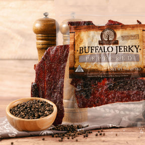 Buffalo jerky strips next to a package with black pepper scattered around, emphasizing the peppered flavor.
