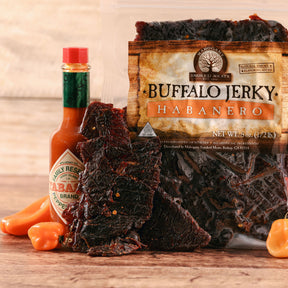 Buffalo jerky and habanero peppers with a bottle of Tabasco sauce on a wooden surface.