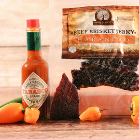 Beef brisket jerky and Tabasco sauce with fresh habanero peppers on a wooden table.