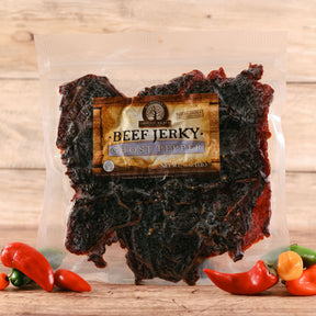Packaged ghost pepper beef jerky with colorful chili peppers on a wooden surface
