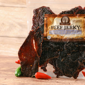 Ghost pepper beef jerky displayed with fresh peppers on wooden surface