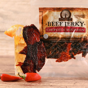 Pack of Chipotle Bourbon Beef Jerky with red chili peppers, displayed on a wooden surface.