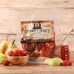 Package of honey turkey jerky with fruits and honey jar on a wooden surface