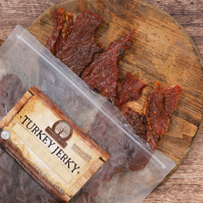 Honey turkey jerky pieces displayed on a wooden board next to its packaging