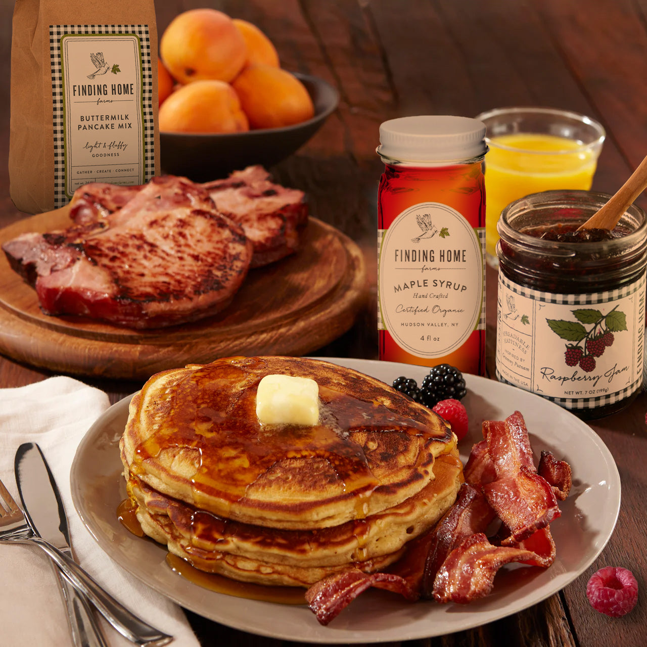A large western breakfast with smoked pork chops, pancakes, smoked bacon, maple syrup and raspberry jam.