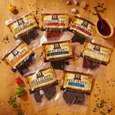 Assorted beef and turkey jerky packs on a wooden surface with spices and sauce.