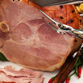 Carved butt half ham with cloves and cinnamon sticks, served with sliced ham pieces.