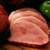 Sliced ham steaks on a wooden board next to a whole ham and a green apple.