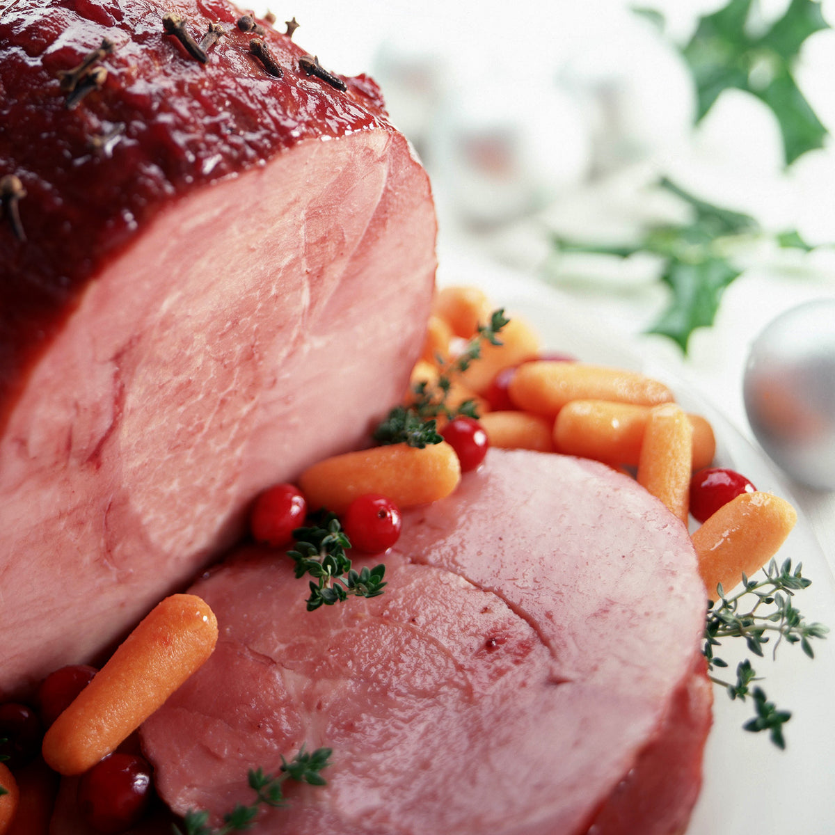 Glazed boneless ham garnished with baby carrots, cranberries, and herbs on a festive table.